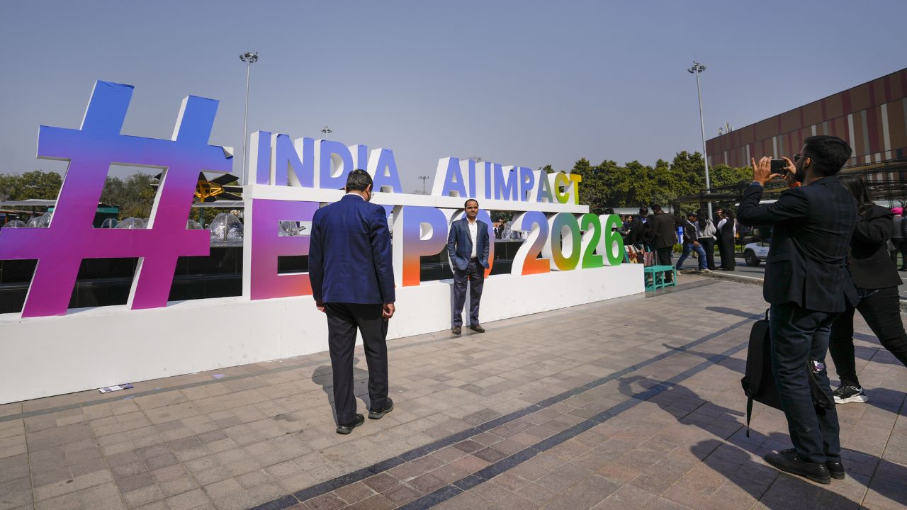 AI Impact Summit के बाहर फोटो खिंचवाते हुए विजिटर । Photo Credit: PTI